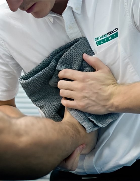 Osteopath stretching a patient's leg with a grey towel